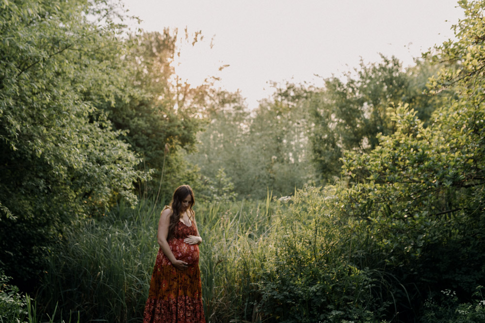 Beautiful image of mum standing in the field and looking down at hew bump. Gorgeous golden hour. Natural photograph showing mum being calm and in the moment. Love to baby bump. Hampshire family photo session. Ewa Jones Photographer