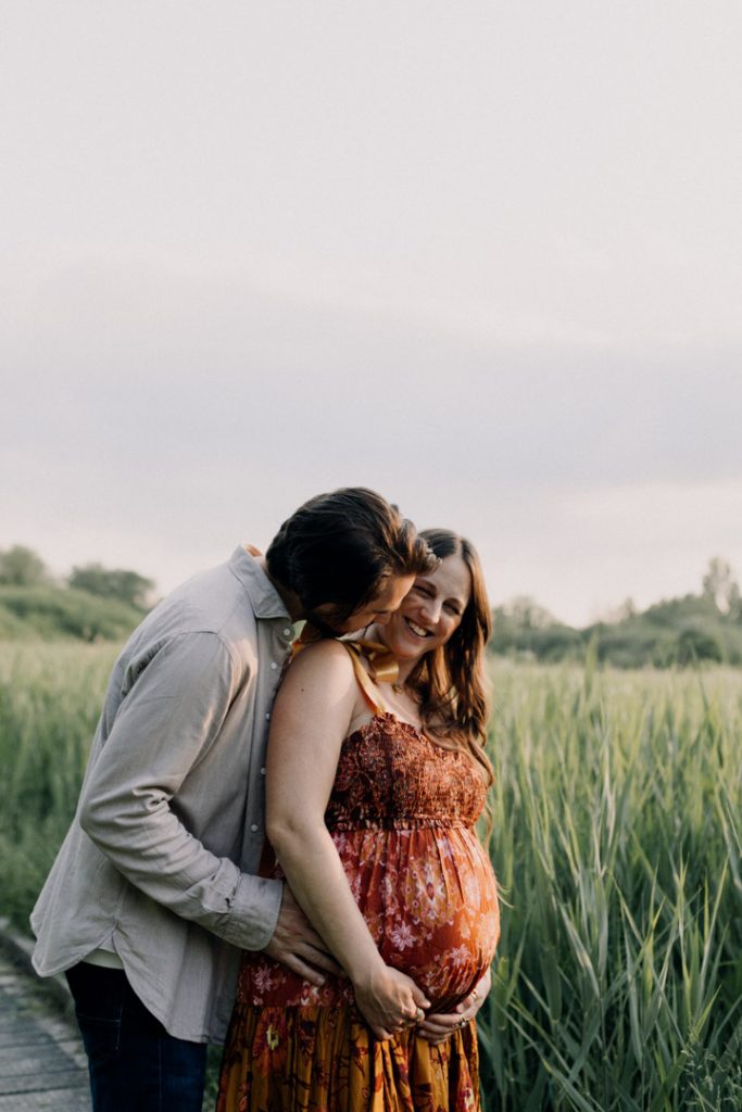 Mum and dad are cuddling and dad is cheekily trying to kiss his wife. playful and natural maternity and bump photo shoot in Winchester. Hampshire photographer.