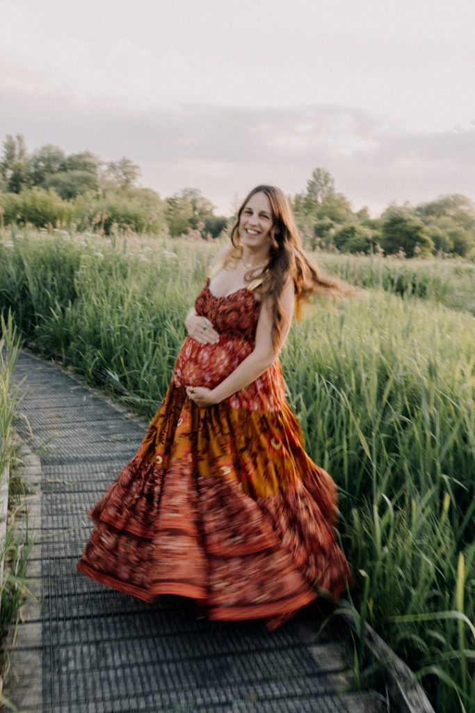 Pregnant woman in a flowing dress walking through a meadow at golden hour, capturing the joy and anticipation of motherhood. Hampshire baby bump photo shoot. Ewa Jones Photography