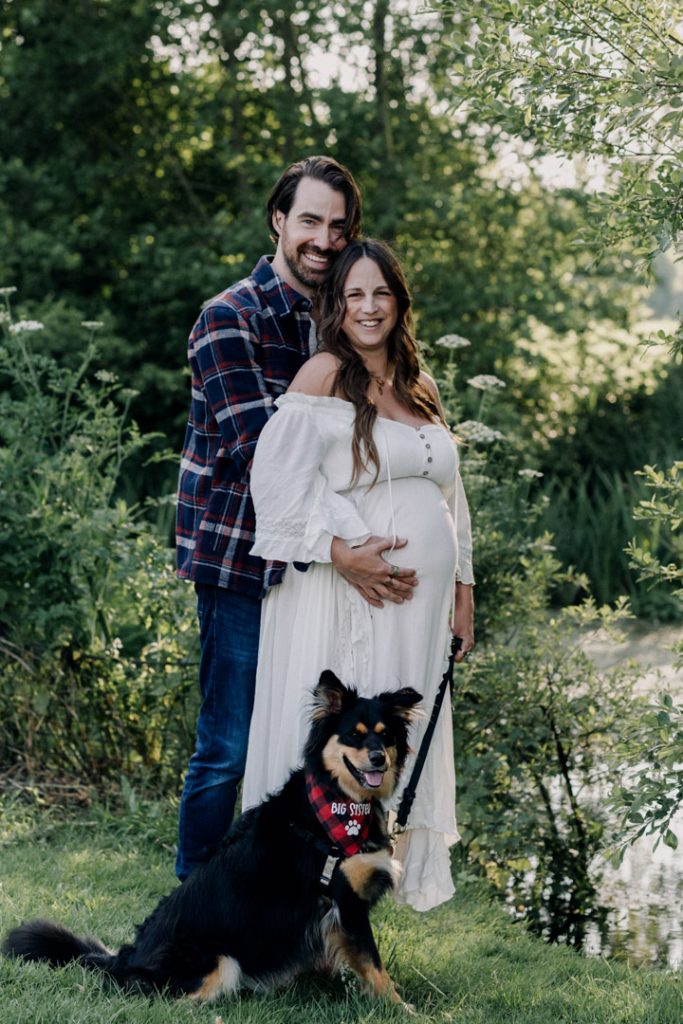 dad and mum to be are cuddling close and looking at the camera. they have their family dog with them. nice bump photo shoot. Hampshire photograper. Ewa Jones Photographer