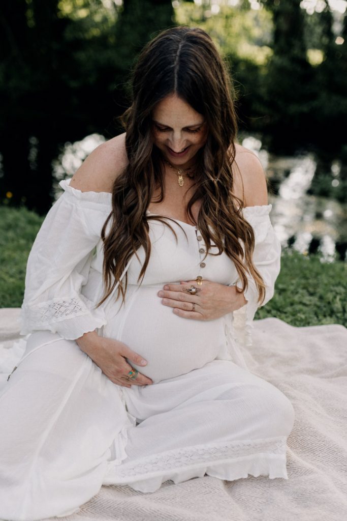 Close up image of mum looking down and holding her baby bump. Hampshire pregnancy photo shoot outdoors. Golden hour photo session. Ewa Jones Photographer