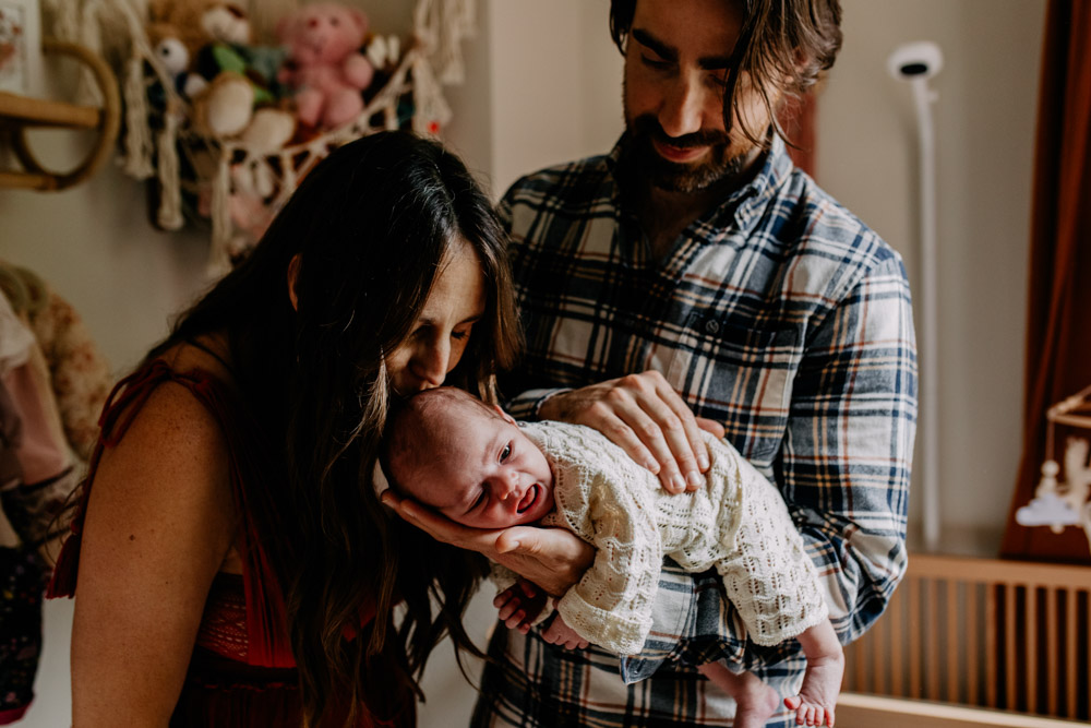 Parents holding their newborn baby during a relaxed lifestyle photoshoot at home, with warm natural light. Ewa Jones Photography