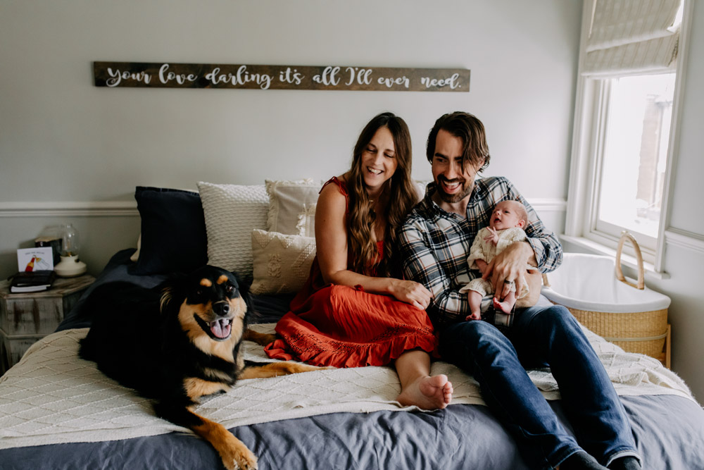 A loving family moment in a Hampshire home as parents sit together with their newborn baby and dog, captured by a Hampshire newborn photographer. Hampshire photo shoot. Ewa Jones Photography