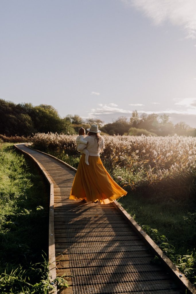 Mum is walking away with her daughter on a wooded path. lovely golden light is lighting up mum's dress. Hampshire family photographer. Ewa Jones Photography
