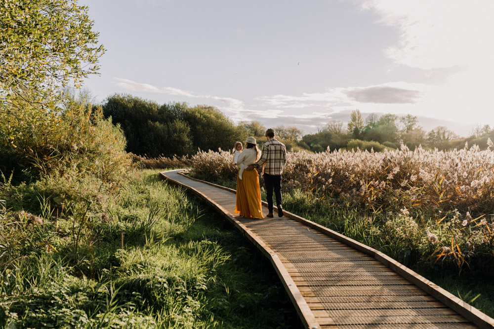 Mum dad and one year old baby girl are walking on the woodland path. beautiful delicate and peaceful photo session. outdoor golden hour family shoot. Hampshire photo shoot. Ewa Jones Photography