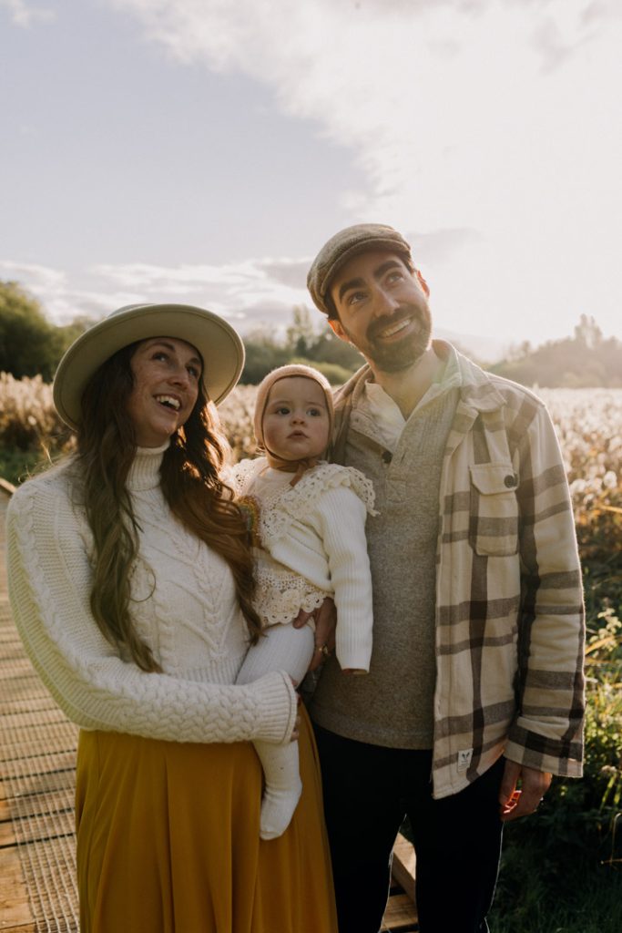 Mum and dad are looking up and smiling. one year old girl is also looking up. golden hour photo session. Basingstoke photographer. Ewa Jones Photography