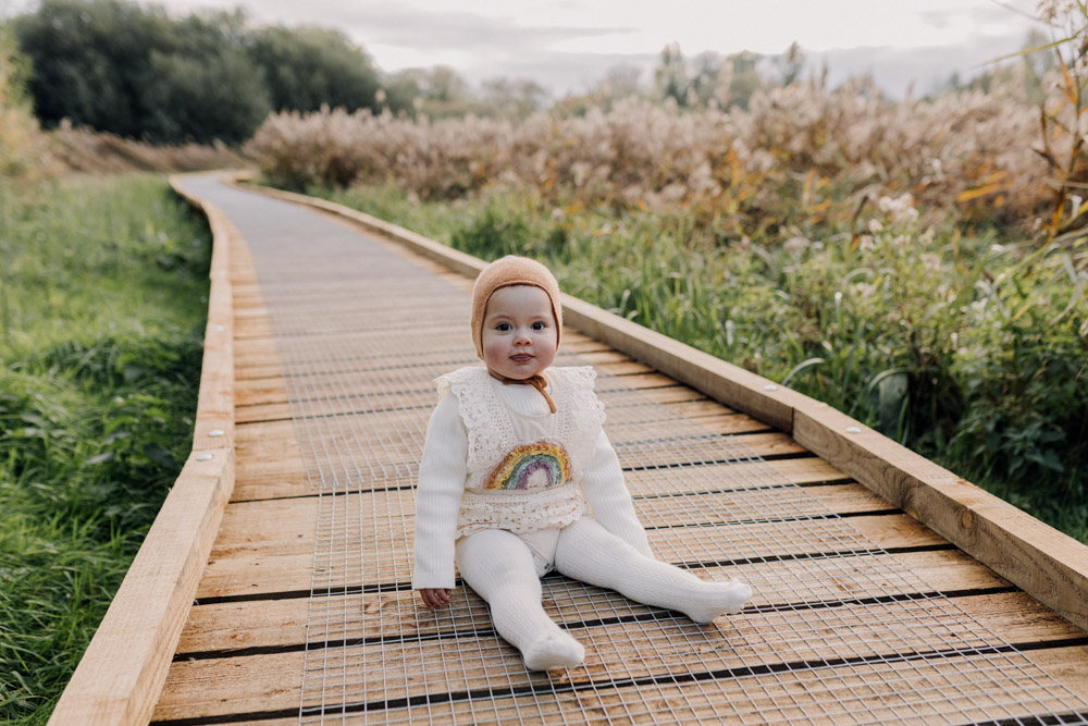 One year old girl is sitting on the wooded path. lovely soft light is behind her. nature common. Winchester family photo shoot. Hampshire photographer. Ewa Jones Photography