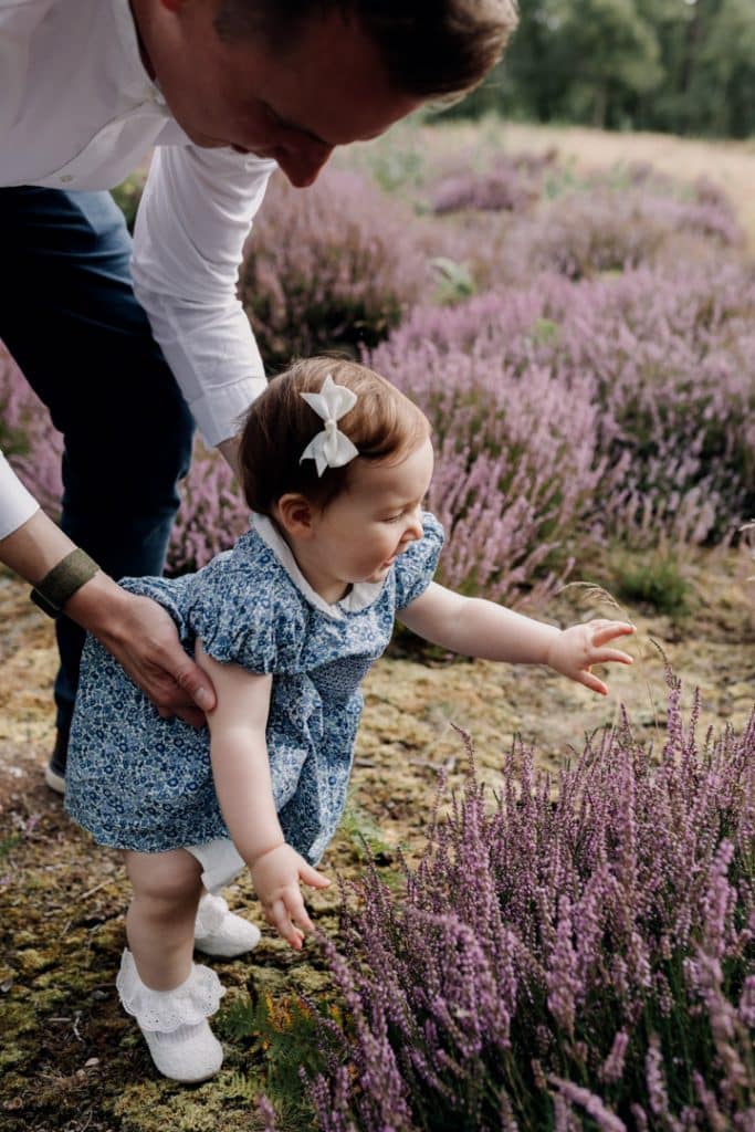 Little girl is on her feet and trying to reach lavender flowers. Celebrating one year old. Natural outside family photo shoot. Hampshire photo shoot. Ewa Jones photography