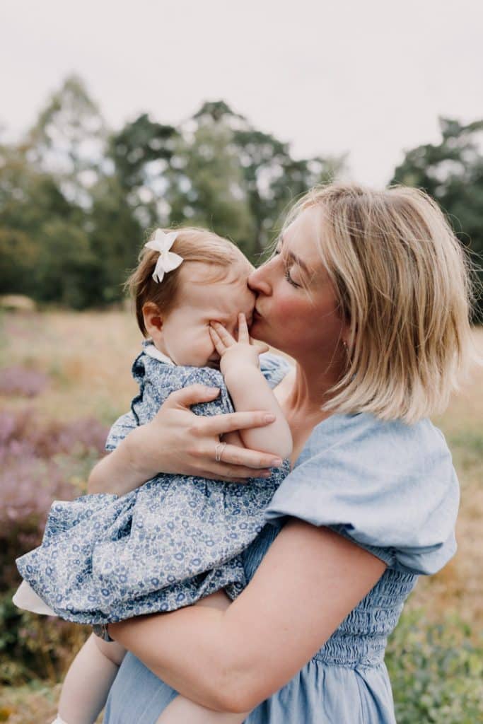 Mum is kissing her daughter and the little girl is hiding her face with her hands. natural image during family photo shoot. Hampshire photographer. Ewa Jones Photography