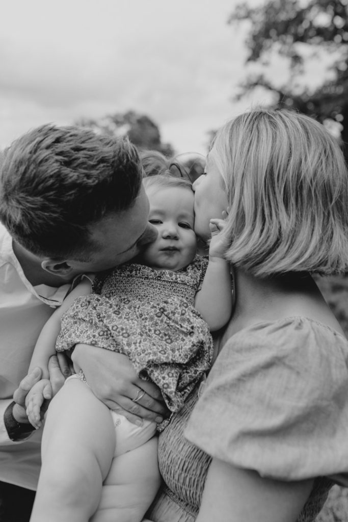 mum and dad are kissing their baby daughter on her face. Hampshire family photo shoot. Hampshire family photographer. Ewa Jones Photography