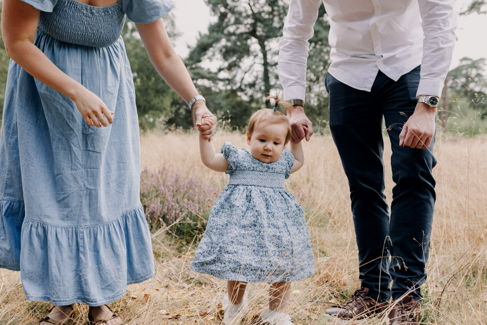 Mum and dad are holding little girls hands and she is trying to walk. Lovely family memories. One year old photo shoot. Hampshire family photo shoot. Ewa Jones Photography