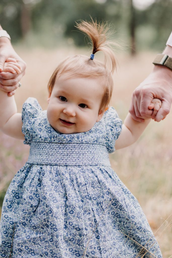 Mum and dad are holding little girls hands and she is trying to walk. Lovely family memories. One year old photo shoot. Hampshire family photo shoot. Ewa Jones Photography