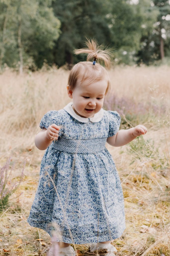 Little girl is standing on the grass and smiling. first steps. First birthday. celebrating one year. family photo shoot. Hampshire photo shoot. Ewa Jones Photography