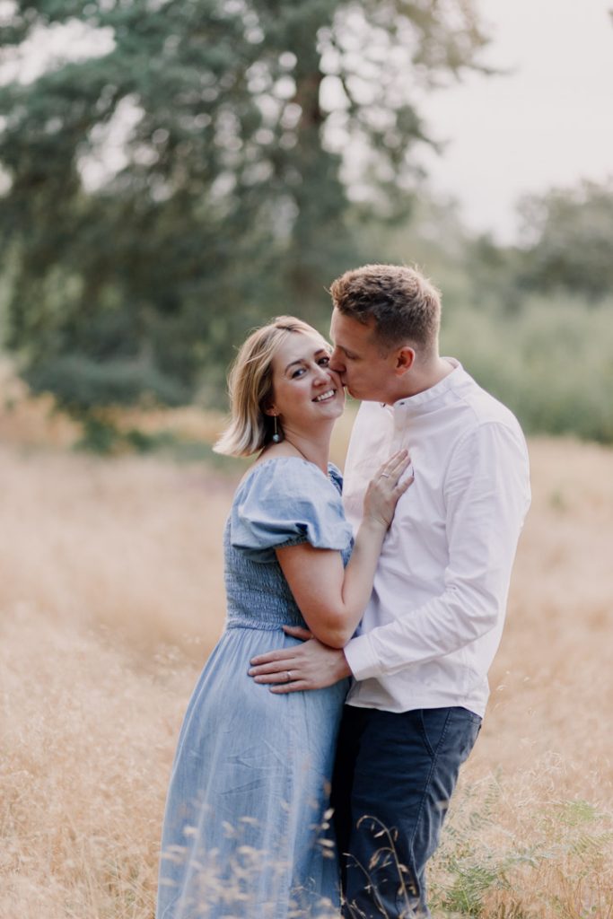 Mum and dad are standing in the field and dad is kissing mum on her cheek. intimate family photo session in Berkshire. Hampshire family photographer. Ewa Jones Photography