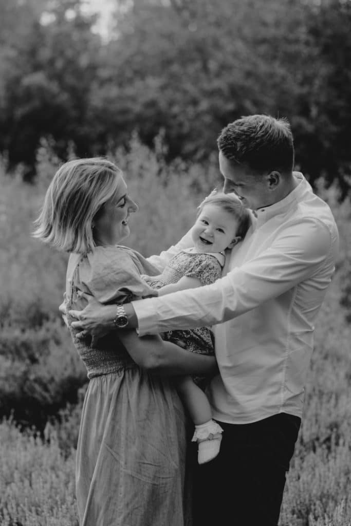 Black and white image of family cuddling each other. Mum and dad are looking at their little girl and smiling to her. Hampshire family photographer. Hampshire photography. Ewa Jones Photography