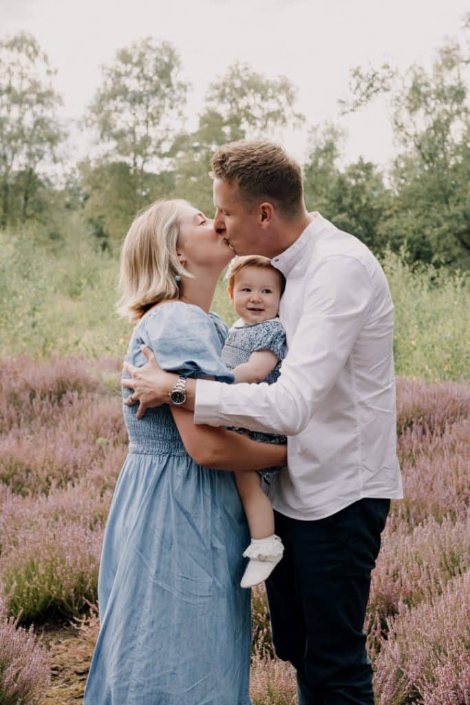 Mum and dad are kissing each other and between them there is their little girl. Lovely natural family photo session in Berkshire. Berkshire family photo shoot. Ewa Jones Photography