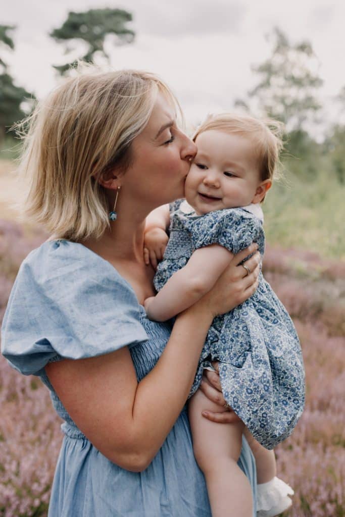 Mum is kissing her daughter on her cheek. Natural family session outdoors. One year old photo session. Family photographer in Hampshire. Ewa Jones photography