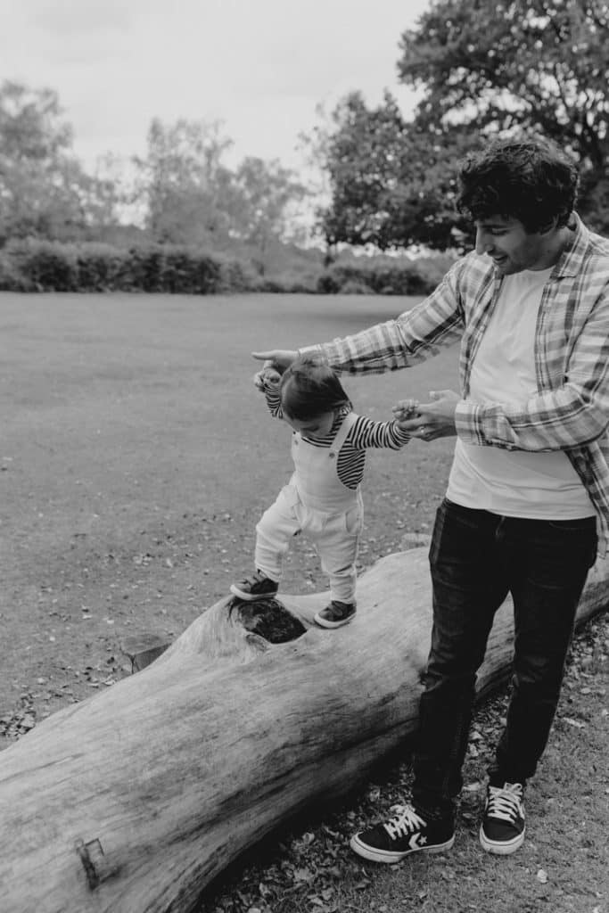 Dad is holding hands of his boy and the boy is walking on the log. family photo session in Hampshire. Hampshire family photographer. Ewa Jones Photography