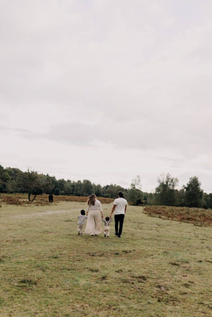 family of four is walking away from the camera, there are horses in the background. New Forest photo shoot. Hampshire family photographer. Ewa Jones Photography