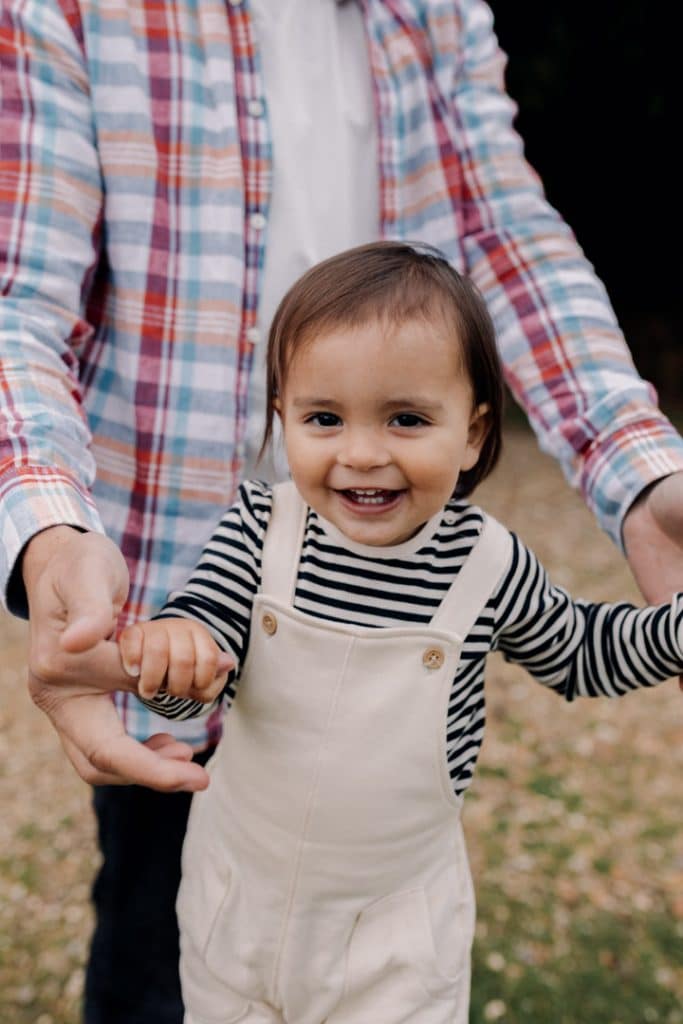 Boy is looking at the camera and smiling. dad is in the background. Natural family photoshoot in Hampshire. Basingstoke family photographer. Ewa Jones Photography