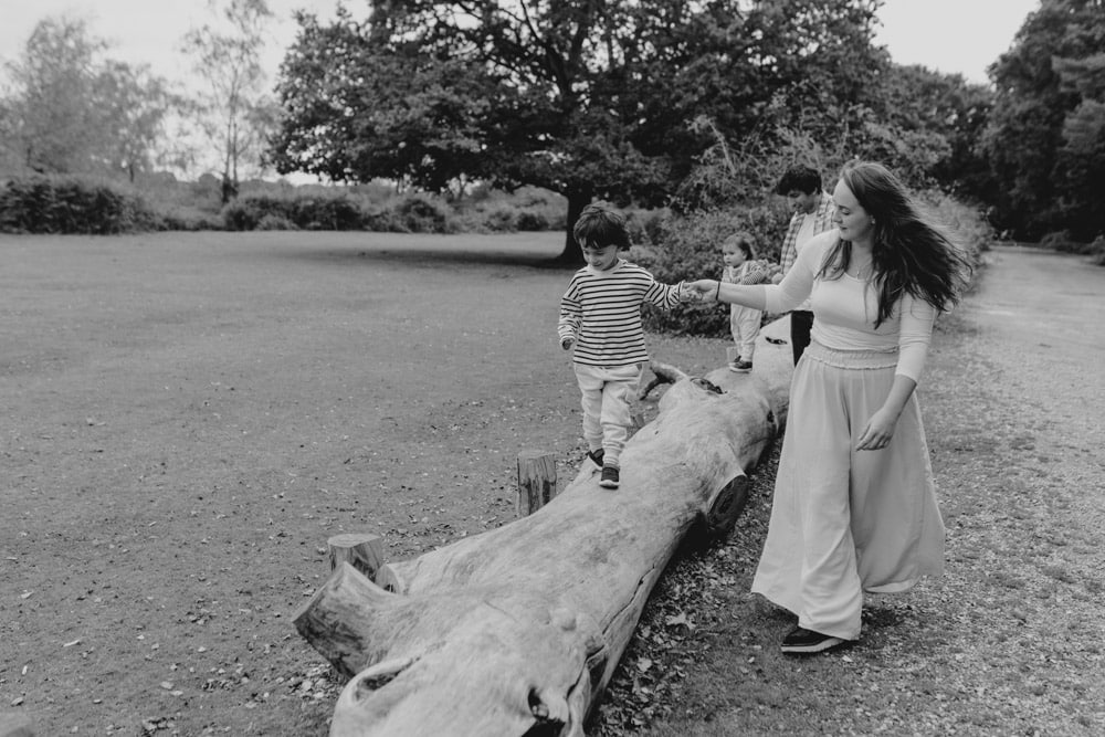 Family of four is enjoying relaxed family photo session. both children are walking on the log. parents are holding their hands. Hampshire photographer. Ewa Jones Photography