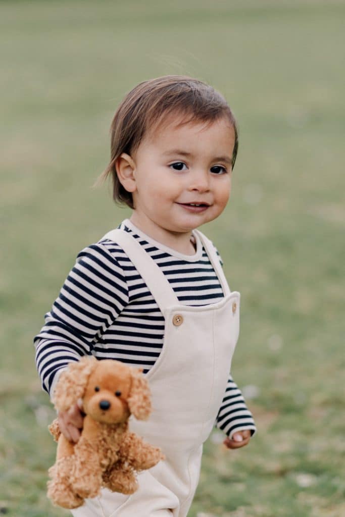 Little boy is looking and holding a toy puppy in his hand. he is wearing stripy top and cream dungarees. Lovely natural family photo shoot in Hampshire. Hampshire family photographer. Ewa Jones Photography