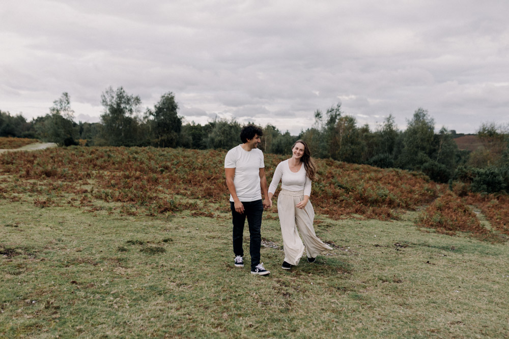 Mum and dad are holding hands and walking towards the camera. Mum is wearing white top and beige trousers. dad is wearing white t-shirt an black trousers. natural family photo session. New Forest family photographer. Ewa Jones Photography
