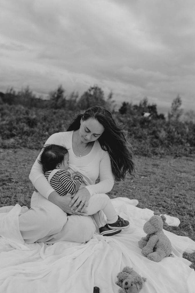 mum is sitting on the blanket and breastfeeding her child. black and white image. capturing moment in life. black and white family images. Ewa Jones Photography