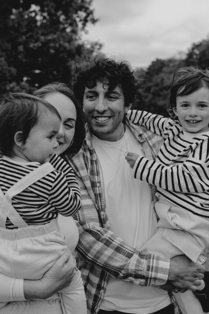 Mum and dad are holding their children and looking at them. children are happy. making memories as a family. un posed family photo session. Family photographer in Hampshire. Ewa Jones Photography