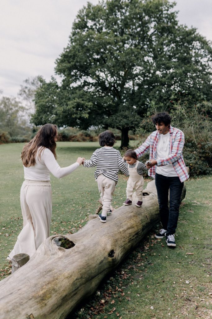 family of four is captured. two boys are walking on the log. Hampshire family photo shoot. new forest photography. dad is holding his son and walking towards wild horses in the New Forest. Hampshire family photo shoot. Family photographer. Ewa Jones Photography
