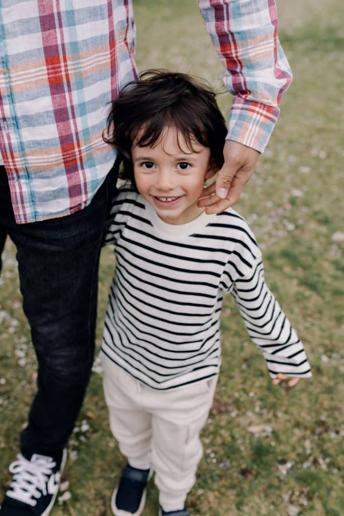 Boy is looking at the camera and smiling. he is wearing stripy top and trousers. dad has his hand on his cheek. natural unposed family photo session in Hampshire. Hampshire family photographer. Ewa Jones Photography