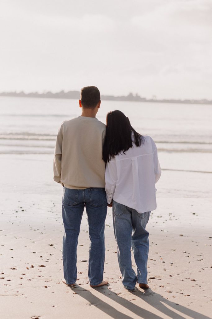 parents to be are standing at the beach and looking into the sea. Maternity photo shoot. Hampshire family photographer. Ewa Jones Photography