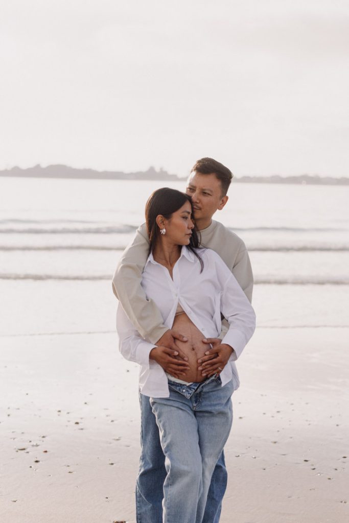 partner is holding his wife and gently kissing her in her temple. maternity photo session at the beach. maternity poses at the beach. Hampshire maternity photographer. Hampshire photographer. Ewa Jones Photography