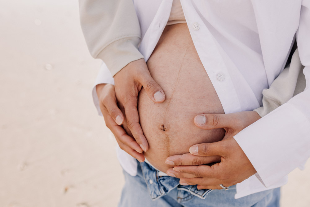 Close up of baby bump being held by both parents. Maternity photo session at the beach. Hampshire family photographer. Bump photo shoot. Ewa Jones Photography