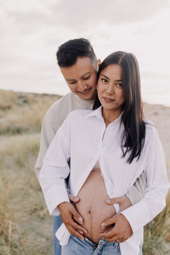 Mum and dad are cuddling. Dad is looking down and mum is looking at the camera. Hampshire maternity shoot. Ewa Jones Photography