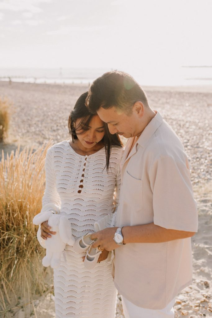 Expecting parents are standing at the beach and looking down at baby bump. lovely summer evening at the beach. What to wear for a maternity photo session. Ewa Jones Photography