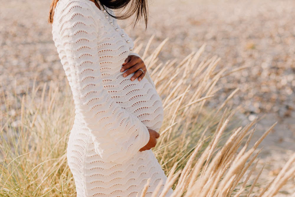 Mum is wearing lovely white dress and standing at the beach. mum to be maternity poses. Hampshire photographer. Ewa Jones Photography