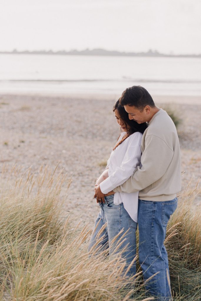 expecting parents are standing at the beach and cuddling to each other. romantic and natural maternity session at the beach. Hampshire family photographer. Ewa Jones Photography
