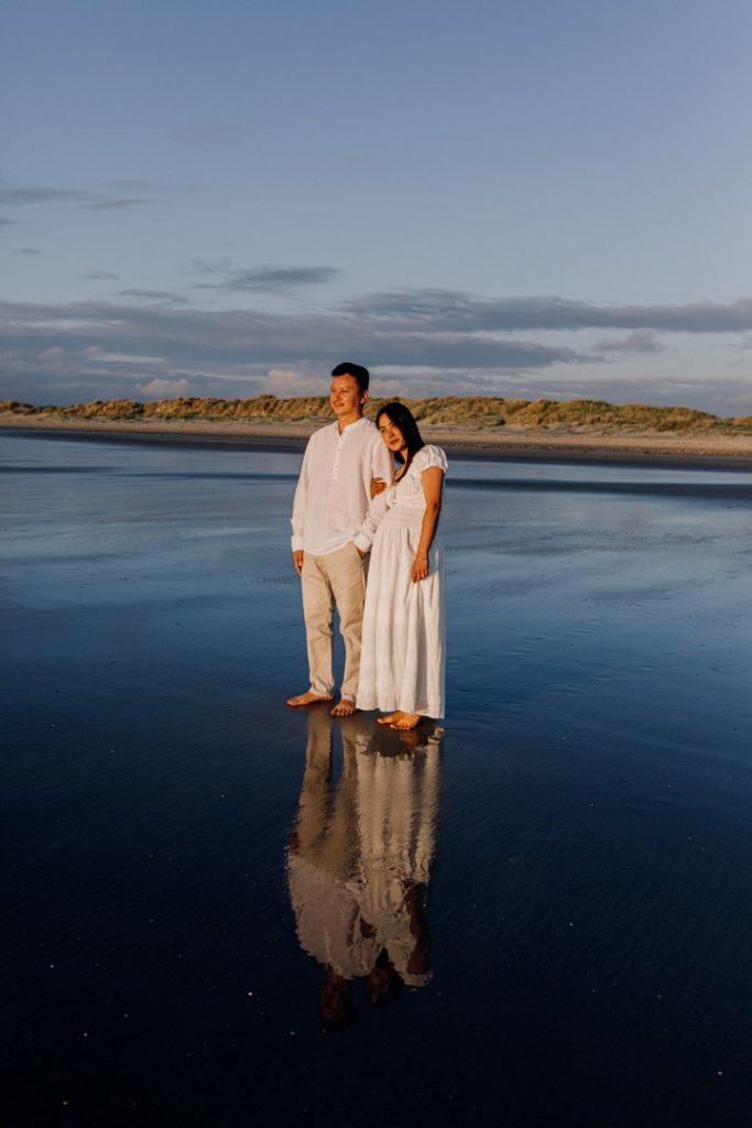 Expecting parents are holding close and looking down at the bump. lovely sun is shining on their bodies. lovely maternity photo session during golden hour at the beach. Hampshire maternity photographer. Ewa Jones Photography