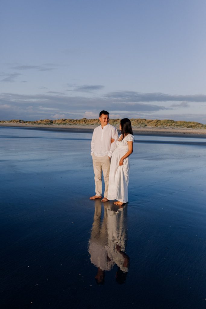 Expecting parents are holding close and looking down at the bump. lovely sun is shining on their bodies. lovely maternity photo session during golden hour at the beach. Hampshire maternity photographer. Ewa Jones Photography