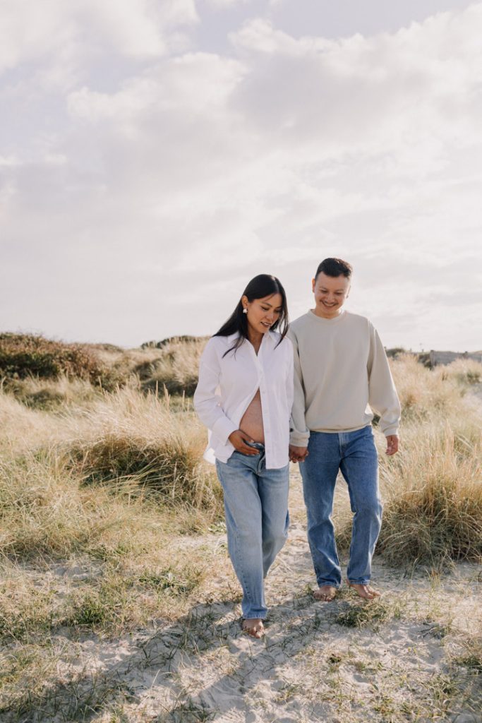 mum and dad are walking at the beach and smiling. natural relaxed maternity photo session. Hampshire family photographer. Ewa Jones Photography