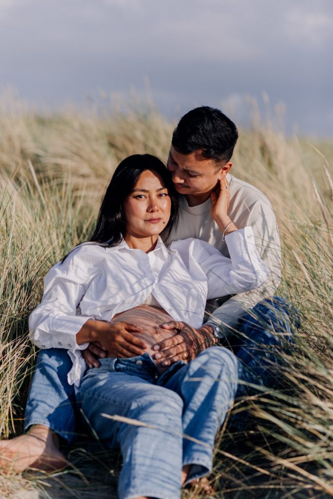 Expecting parents are relaxing at the beach. mum is looking at the camera. lovely romantic authentic maternity session. Hampshire photographer. Ewa Jones Photography
