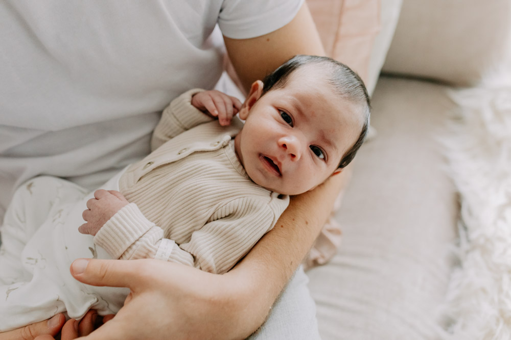 Newborn baby is being held by dad and looking at the camera. lovely natural photo session in Hampshire, Hampshire newborn photo shoot. Ewa Jones Photography