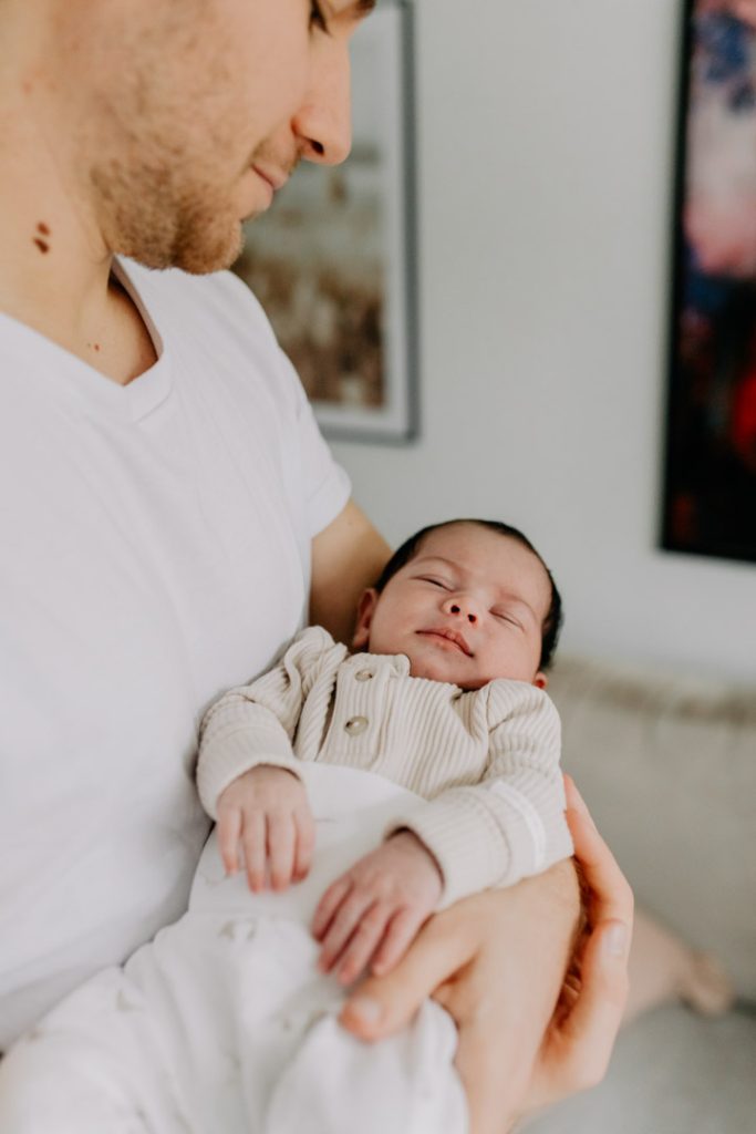 Dad holding his peacefully sleeping newborn baby during a natural in-home newborn photo session in Hampshire. Ewa Jones Photography