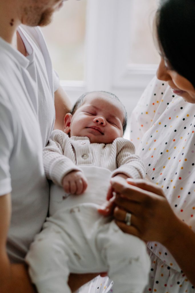 Parents gently holding their peacefully sleeping newborn baby during an in-home newborn photo session in Hampshire. Ewa Jones Photography. Hampshire photographer