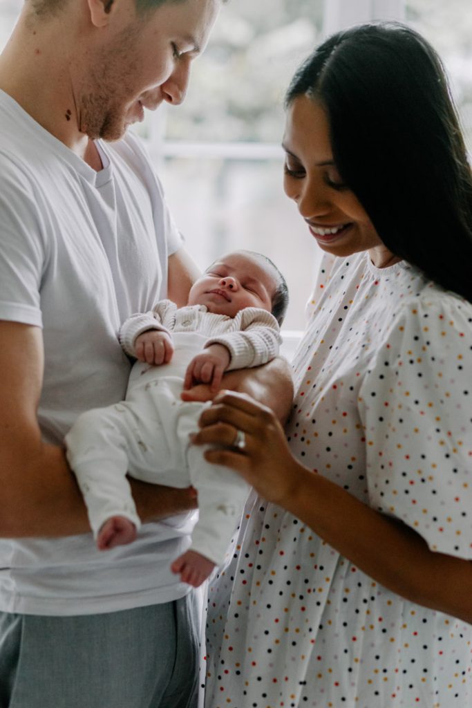 Parents gently holding their peacefully sleeping newborn baby during an in-home newborn photo session in Hampshire. Ewa Jones Photography. Hampshire photographer