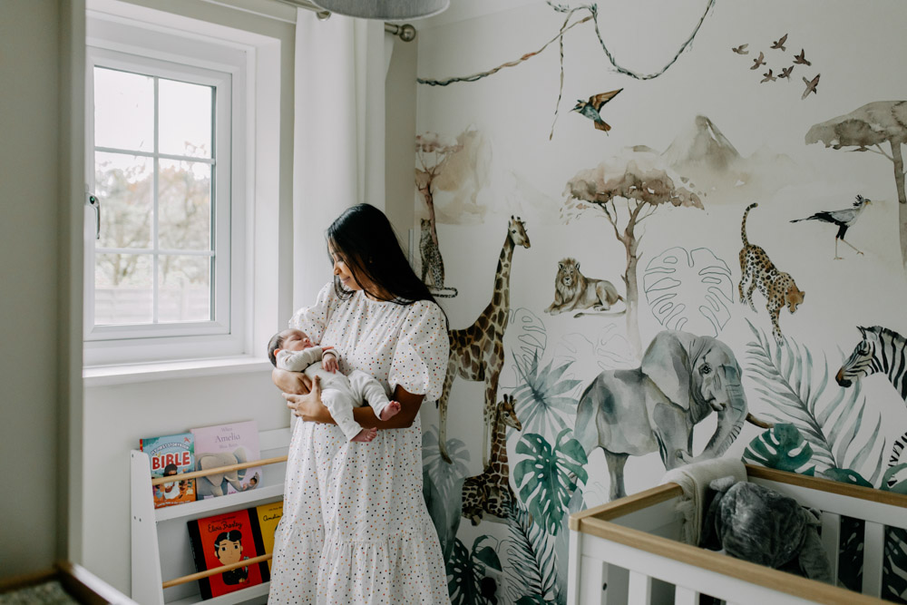 mum is standing in the baby nursery and looking down at her newborn baby. lovely natural baby nursery with safari theme. Hampshire newborn baby photo shoot. Ewa Jones Photography. A Beautiful In-Home Newborn Photo Session in Hampshire