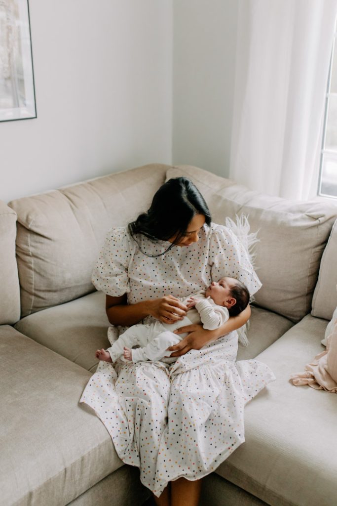 mum is sitting on the sofa and looking down at her baby. natural in home settings. Mum is wearing lovely dress and baby is in natural colours. Newborn photo session in Hampshire. Hampshire newborn photographer. Ewa Jones Photography