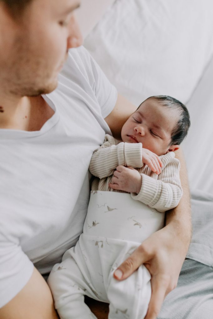 Dad is holding newborn baby and looking at the baby. Newborn photo shoot in Hampshire. Ewa Jones Photography