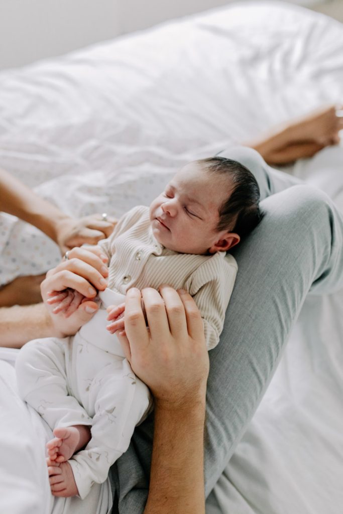baby is laying on dads legs and sleeping. baby is wearing cream colors on the clothing. Hampshire newborn photographer. Ewa Jones Photography